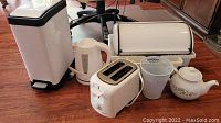 Photo shows all items in lot together: waste can, kettle, toaster, bread box, teapot, dish drainer on wood floor.