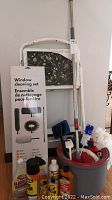 Photo shows unopened window cleaning set, stepladder, red-rimmed bucket with cleaning brushes and mop inside.