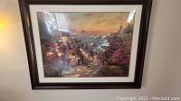 Full view of large framed Thomas Kinkade print showcasing a coastal village at sunset with lighthouse in background.