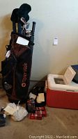 Full view of TaylorMade golf bag with multiple clubs, Coleman cooler, golf balls, shoes, and umbrella placed on floor.