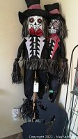 Two Halloween scarecrows standing against a wall, showing full body and attire details with skeleton designs and red bow ties.