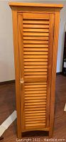 Front view of tall wood cabinet with louvered door and glass knob