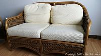 Full frontal view of bamboo and wicker loveseat with white cushions on seat and backrest.