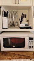 Kitchen utensils in holders including knives and various metal kitchen tools above RCA microwave