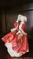 Photo of Royal Doulton porcelain figurine of a woman in a red dress and white hat, showing front side.