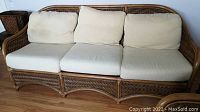 Frontal view of bamboo wicker three-seater sofa with three beige cushions