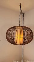 Front view of the swag lamp hanging from ceiling, showing full rattan basket spherical shape and glowing plastic inner shade.