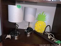 Pair of chrome base table lamps with white fabric shades and pineapple battery wall light on shelf