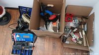Overall view of multiple boxes containing various hand tools, power tools, and hardware items.
