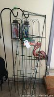 Four green wire trellises with two shepherds hooks holding two hanging lanterns and a flamingo garden statue at the base.