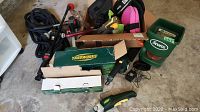 Boxed Yardworks cordless shears, pruners, Scotts spreader, kneepads, garden tools in garage floor setting