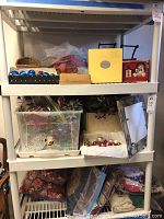 Wide view of plastic bins, boxes, and holiday decor items on shelving including ornaments, ribbons, and linens