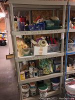 Four shelves filled with assorted painting supplies including rollers, masking tape rolls, paint cans, buckets, brushes, and other tools.
