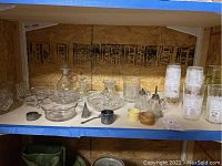 Shelf with antique glassware including nut dishes, oil and vinegar bottles, small bowls, silver plate spoon and napkin ring, tall glasses with white glaze and gold plating.