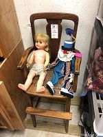 Wooden high chair with cane seat and lucite protector, showing front with plastic doll and fabric clown seated.