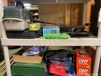 Shelving unit displaying assorted camping and barbecue gear including boxed OFF! Power Pads, fishing tackle box, tools and grilling accessories.