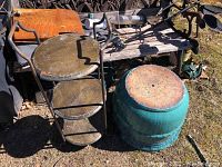 Outdoor setting showing large turquoise glazed clay pottery flower pot next to black metal 3-tier stand on grass near wooden bench.
