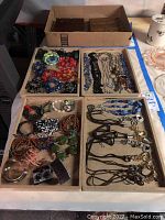 Overview photo showing multiple trays of costume jewelry including bracelets, necklaces, and earrings in various styles and colors.