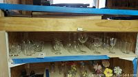 Shelf with a variety of clear crystal and glass stemware including goblets and wine glasses, serving bowls or dishes, and a few salt and pepper shakers.