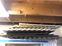 Photo of a horizontal stack of interlocking floor mats in dark colors stored under a wooden beam ceiling.