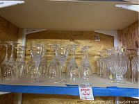 Wide view of multiple crystal wine glasses and water glasses arranged on shelves, showing style and quantity of glassware.