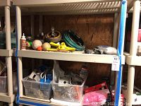 Two-tier plastic shelves with various yard and electrical items including hoses, sprinklers, nylon rope, electrical parts in bins and loose on shelf surface.