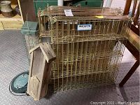 Photo shows three gold-colored metal pet fence sections stacked together with a Precision label visible. Four bird feeders are arranged nearby: one tall green cylindrical feeder with a cage and metal tray, one round green mesh feeder, and a wooden bird feeder with a roof showing wear.