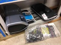 Gray HP Photosmart 8400 photo printer on shelf next to black Epson V500 Photo scanner. Accessories sealed in plastic bag below.