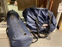 Two dark blue nylon bags, one cylindrical, one zippered with tent fabric and poles inside.