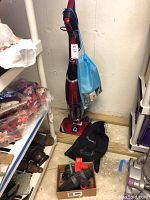 Full view of the red Quantum X upright vacuum cleaner with accessories including black pouch and blue cloth bag, placed on the floor.