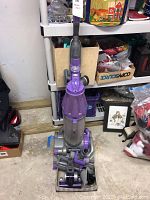 Bottom to top angled front view of Dyson vacuum on floor showing overall vacuum and attachments in front.