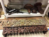 Wood carved wall hangings and wood wall sconces along a shelf for display.