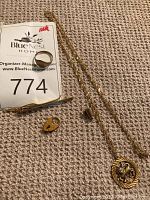 Overview of chain, ring, charms and tie clip on carpet with lot marker
