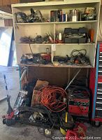 Wide view of white shelving unit holding various power tools with Craftsman arc welder on floor below