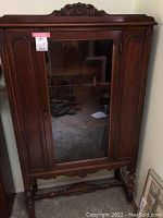Front view of the armoire centered in the photo showing ornate wood carvings and central glass door with visible shelves inside.