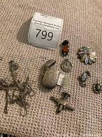 Full view of assorted silver jewelry including the amber cat pendant, engraved locket, seahorse pendant, goddess pendant, starburst pin, and several chains on a beige textured surface.
