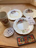 Photo showing an assortment of commemorative plates, mug, and tins on a wooden surface under window light.