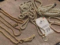 Overall assortment of pearl and pearl-look necklaces on carpet with auction lot card visible