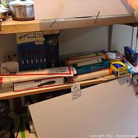 Photo showing various kitchen tools, parchment paper, and Kirkland aluminum foil on a wooden shelf.