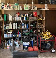 Wooden shelf with multiple cubby holes holding chemical jugs, spray cans and small parts; generator visible at bottom right