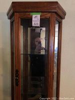 Front view of tall wood and glass tiered cabinet with visible door and hardware.