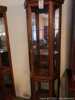 Front and side view showing wooden frame with glass panels, door with knob, and interior glass shelves.