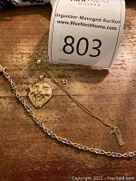 Rope chain necklace, devil-face pendant and bracelet on wood surface with auction label