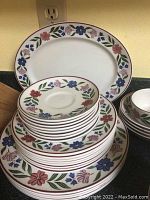 Stack of floral dinner plates, saucer plates, and smaller plates with multi-colored flower and leaf trim on white backgrounds