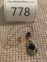Full view of rose gold chain laid flat with pendant on carpet beneath lot number card