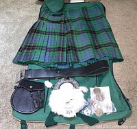 Overview of green and blue tartan kilt and accessories laid on case