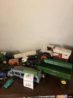 Overview of toy tractors and trucks showing white and red tractor, green trailer wagon with yellow wheels, Dinky Toys delivery bus, and several toy vehicles.