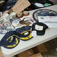 Three embroidered caps at front, mugs, patches and board signs behind