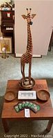 Photo showing tall wooden giraffe standing on wooden coffee table with coasters, bowls, and candleholder arranged on table.