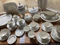 Overall lot of white bone china pieces arranged on wooden surface by window